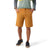 A person stands with hands in pockets, wearing mustard-colored Smartwool Mens 10 Inch Short, a long-sleeve green and gray shirt, and black sneakers with white soles against a plain white background.