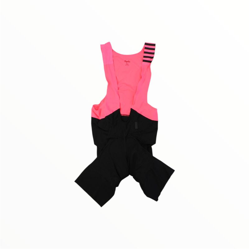 A pair of Rapha Mens Pro Team Bib Shorts II - Regular with a bright pink upper, black lower section, and left shoulder strap featuring black horizontal stripes, shown flat on a white background. Includes a race-grade chamois for comfort.
