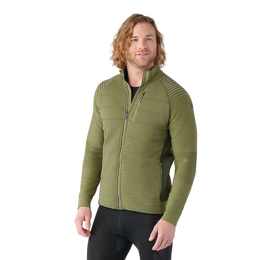 A man with long, wavy blonde hair models the Smartwool Men's Intraknit Merino Insulated Jacket in olive green, featuring ribbed detailing on the shoulders and sleeves, standing against a plain white background.