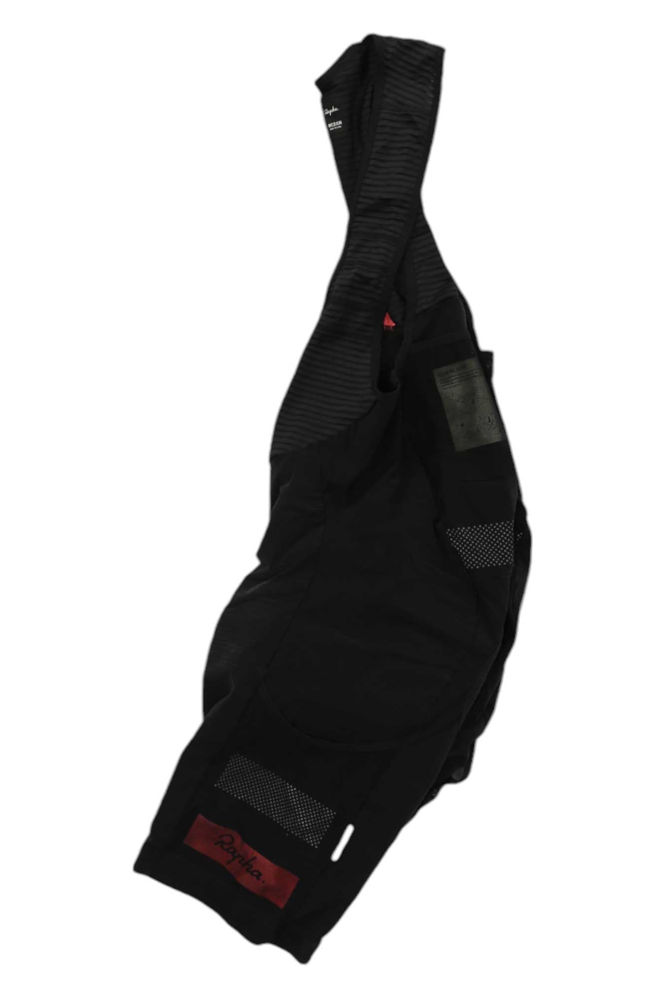 A pair of Rapha Cargo Bib Shorts in black, featuring mesh panels, dense-knit fabric for cycling comfort, shoulder straps, and small red and green patches, shown on a plain white background.