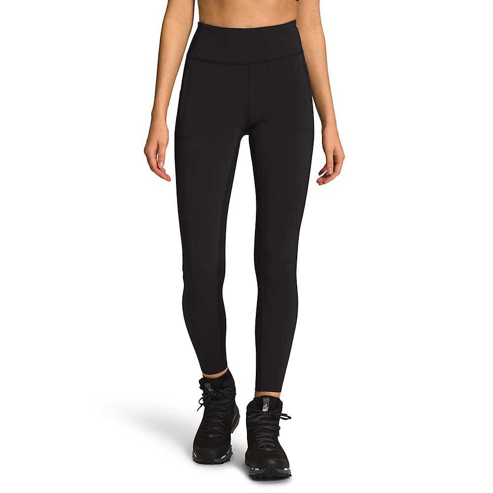 A person wearing The North Face Womens Bridgeway Hybrid Tight, which are high-waisted black fitness pants with an adjustable waist, and black athletic shoes stands against a white background. Only their midsection and legs are visible.