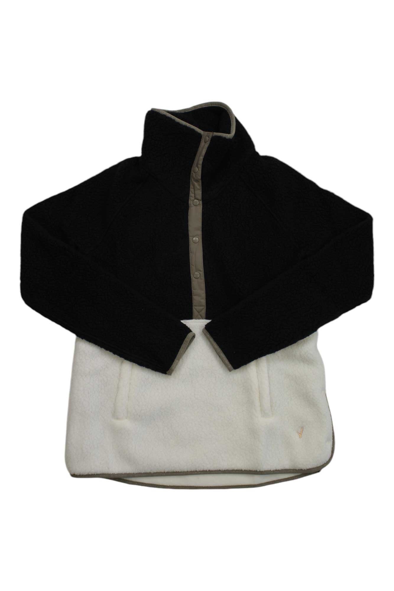 The Indyeva Womens Pecora CB Jacket is a long-sleeve Polartec fleece pullover with a black upper, white lower, high collar, button-up neck, and two front pockets—perfect for outdoor adventures.
