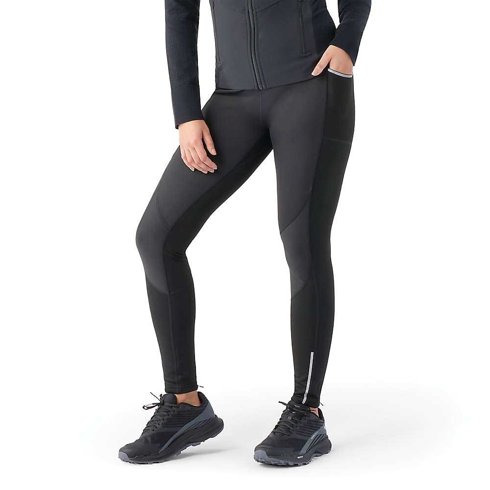 A person is wearing Smartwool Womens Active Fleece Wind Tight, a black zip-up jacket, and black running shoes while standing against a plain white background. Their face is not visible and their arms are relaxed.