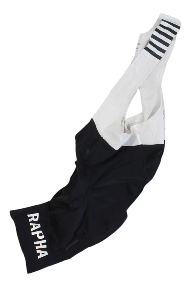 The Rapha Mens Pro Team Bib Shorts II - Regular are black and white cycling bib shorts with "RAPHA" on the left leg and black stripes on the white shoulder strap, featuring a race-grade chamois, shown laid flat on a white background.