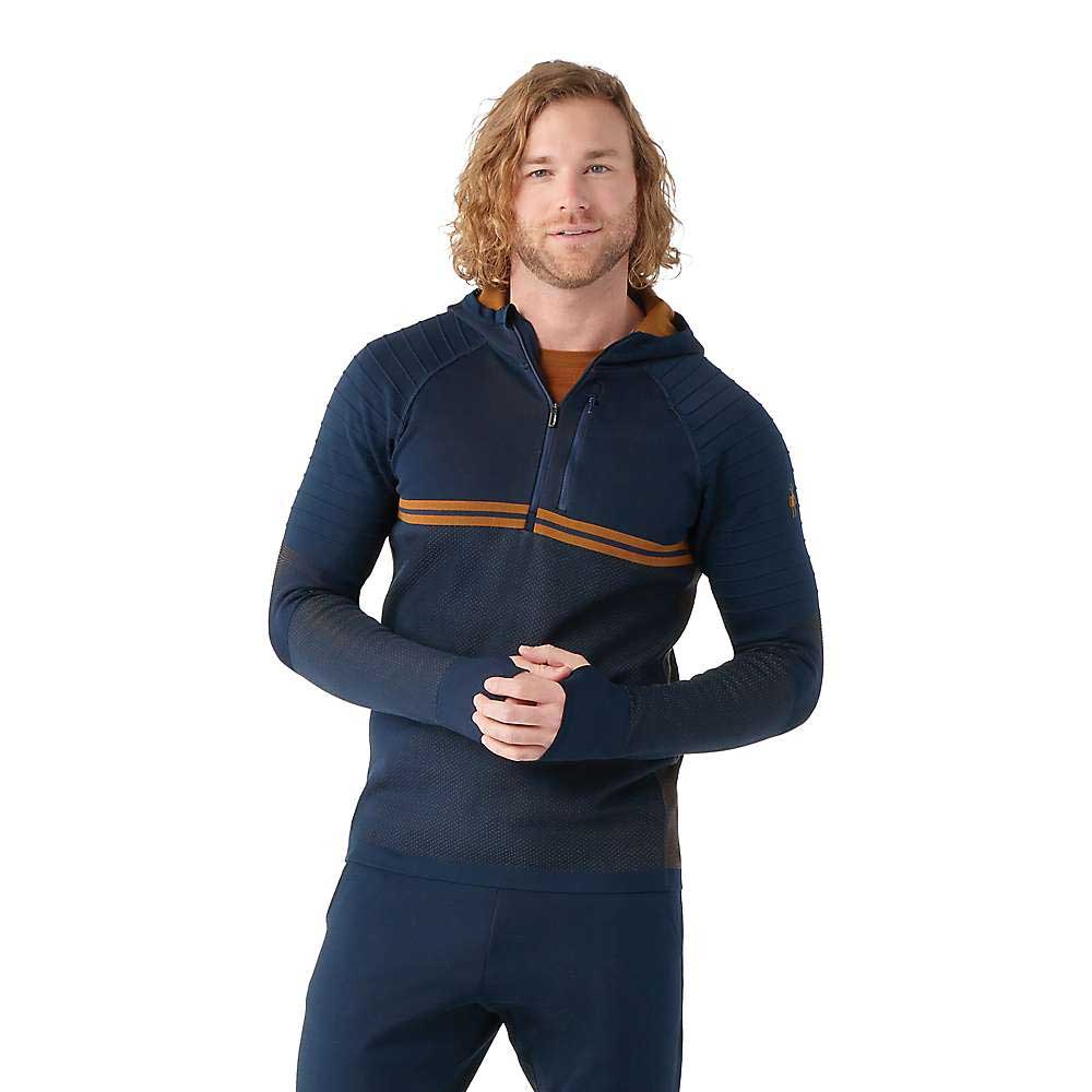 A man with wavy, shoulder-length hair wears a navy Smartwool Mens Intraknit Merino Tech 1/2 Zip Hoodie with an orange stripe, designed for outdoor activity, standing against a plain white background.