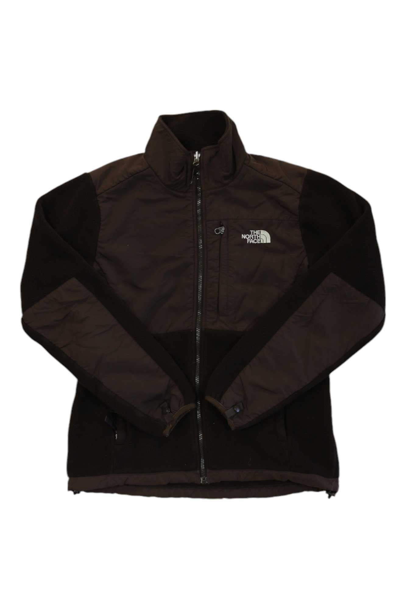 The Denali Jacket is a women's fleece by The North Face in black and dark brown, featuring long sleeves, side pockets, a stand-up collar, and the logo on the left chest. Made from recycled fleece for added sustainability.