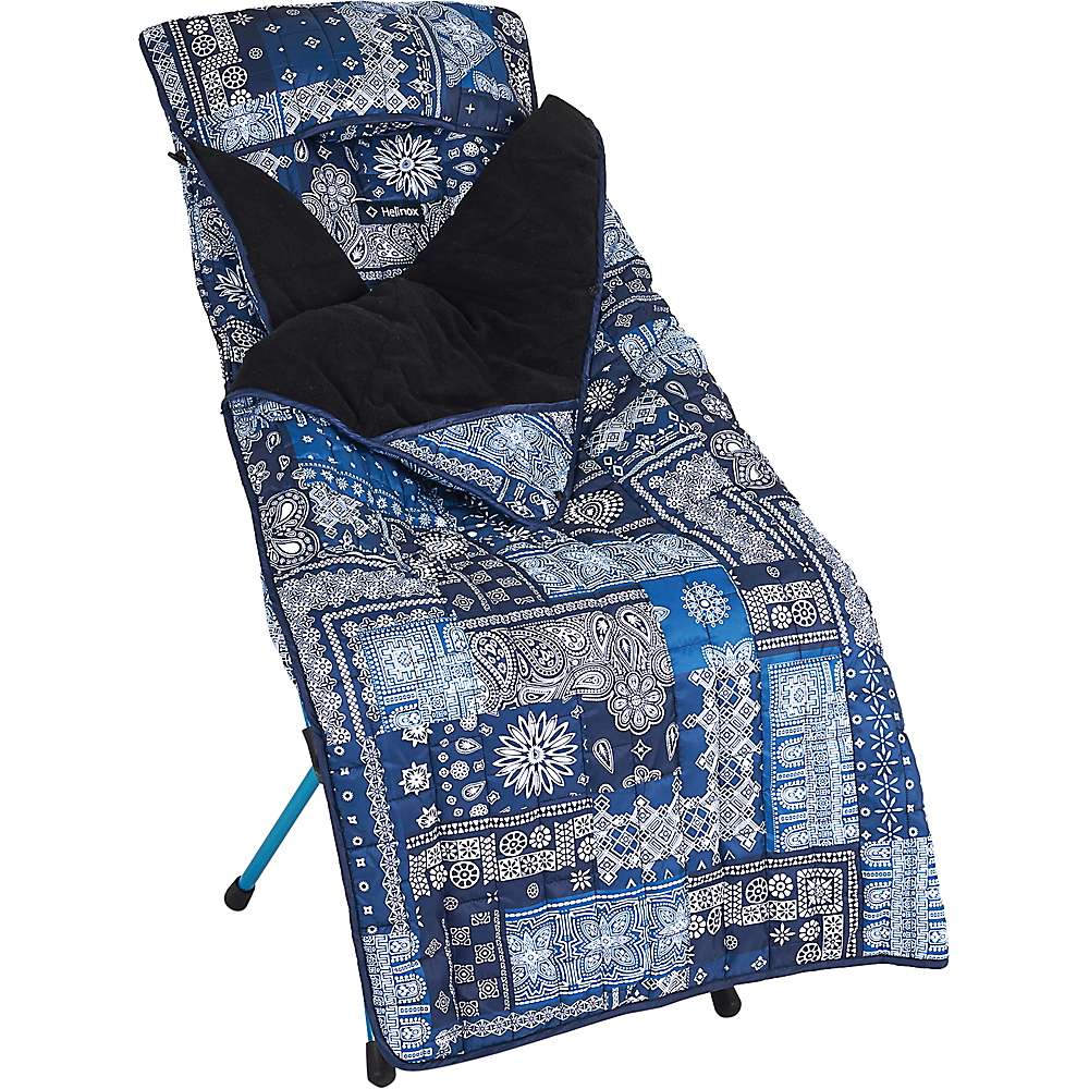 A blue and white patterned sleeping bag with a black interior lining, laid out on a blue folding cot, pairs perfectly with the Helinox Toasty Blanket for Sunset/Beach for extra warmth.