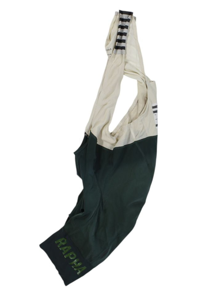 A pair of Mens Bib Shorts in green and cream, with RAPHA in green on the left leg and black stripes on cream shoulder straps, laid flat on white—an eye-catching piece of men's cycling apparel.
