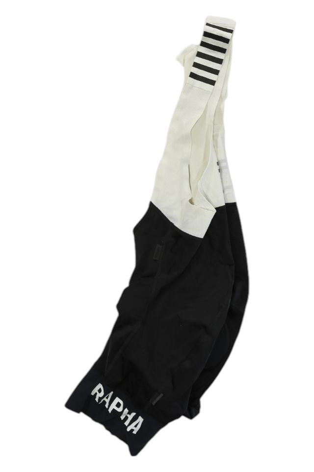 The Rapha Mens Pro Team Bib Shorts II - Regular feature a race-grade chamois, black and white design, RAPHA logo on one leg, and white straps with black stripes, shown laid flat on a white background.
