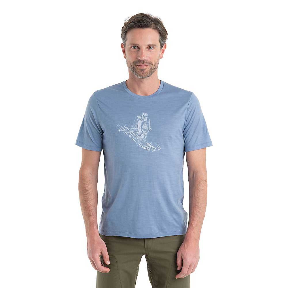 A man with short brown hair and a trimmed beard wears the Icebreaker Mens Tech Lite II SS Tee - Skiing Yeti in light blue and green pants, standing against a plain white background.