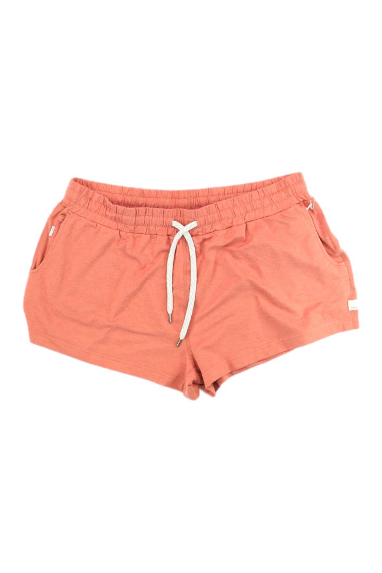 Vuori Women's Halo Performance Shorts in coral pink feature an elastic waistband, white drawstring, and side pockets. Made from moisture-wicking recycled materials, the shorts are shown laid flat on a white background.