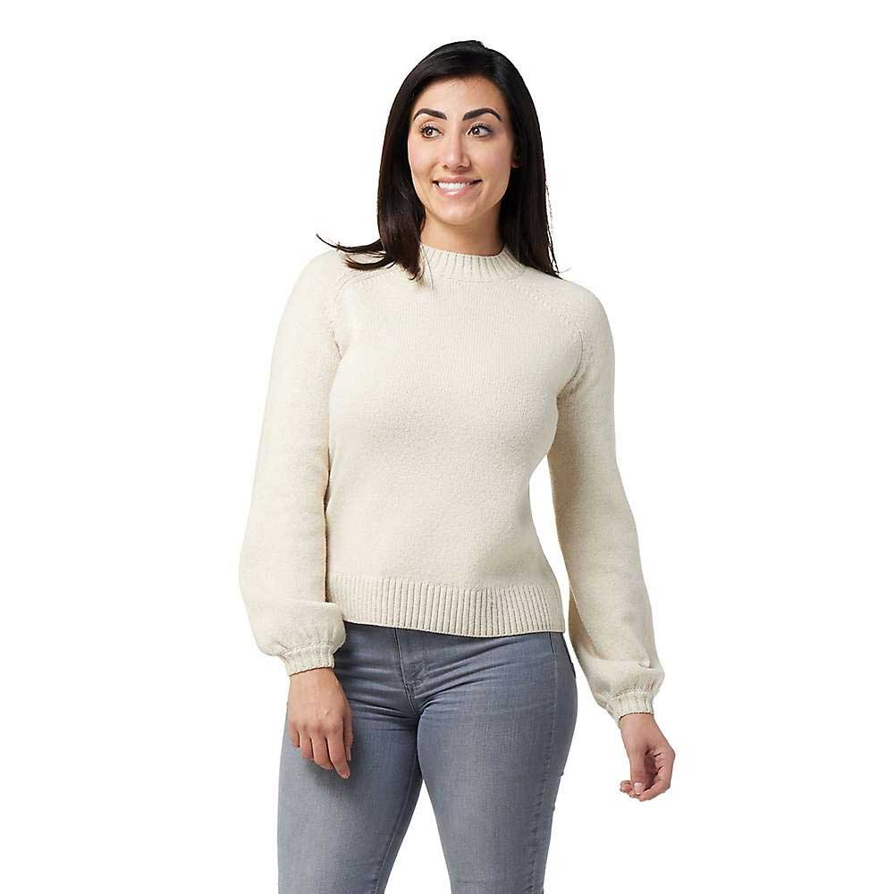 A woman with long dark hair smiles against a white background, wearing the Smartwool Women's Cozy Lodge Bell Sleeve Sweater in cream paired with gray jeans.