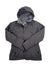 The gray Women's Jet Set Jacket features synthetic insulation, a hood, high collar, waterproof fabric, front zipper with button closure, and two front pockets. Displayed flat with crossed sleeves.