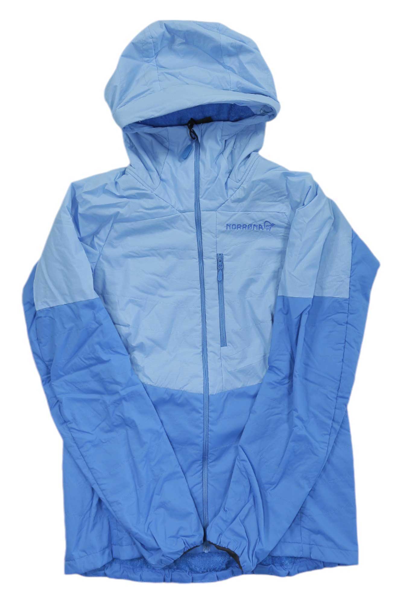 The Norrona Womens Lyngen Alpha100 Zip Hoodie, shown in light and medium blue color-blocks with a front zipper and chest pocket, is laid flat with sleeves crossed at the bottom.