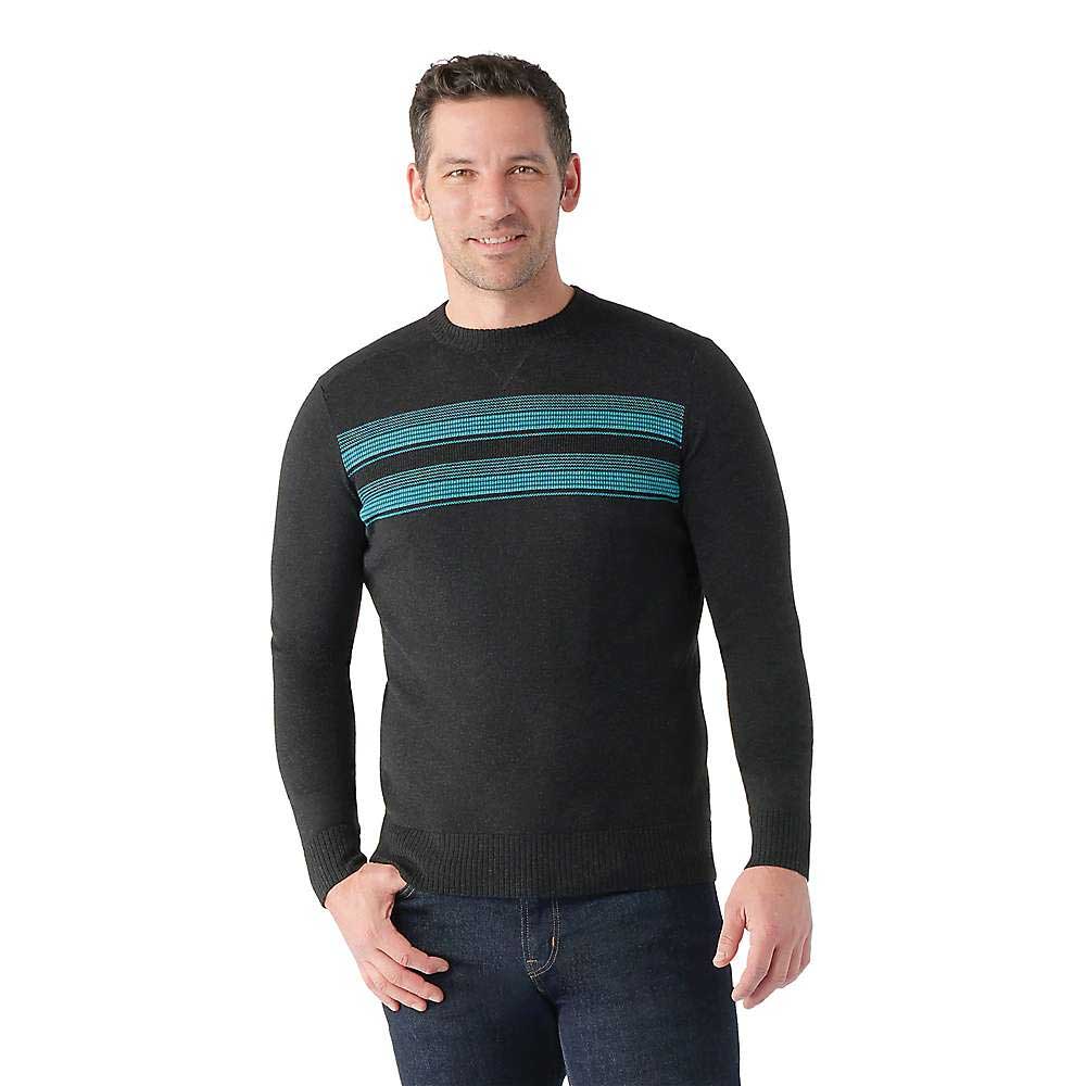 A man smiles against a white background wearing the Smartwool Mens Sparwood Stripe Crew Sweater, featuring horizontal teal and blue stripes across the chest, made from soft Merino wool, paired with dark jeans.