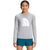 A girl stands smiling in a light gray The North Face Girls Amphibious LS Sun Tee with a large white logo on the front and teal shorts, set against a plain white background.
