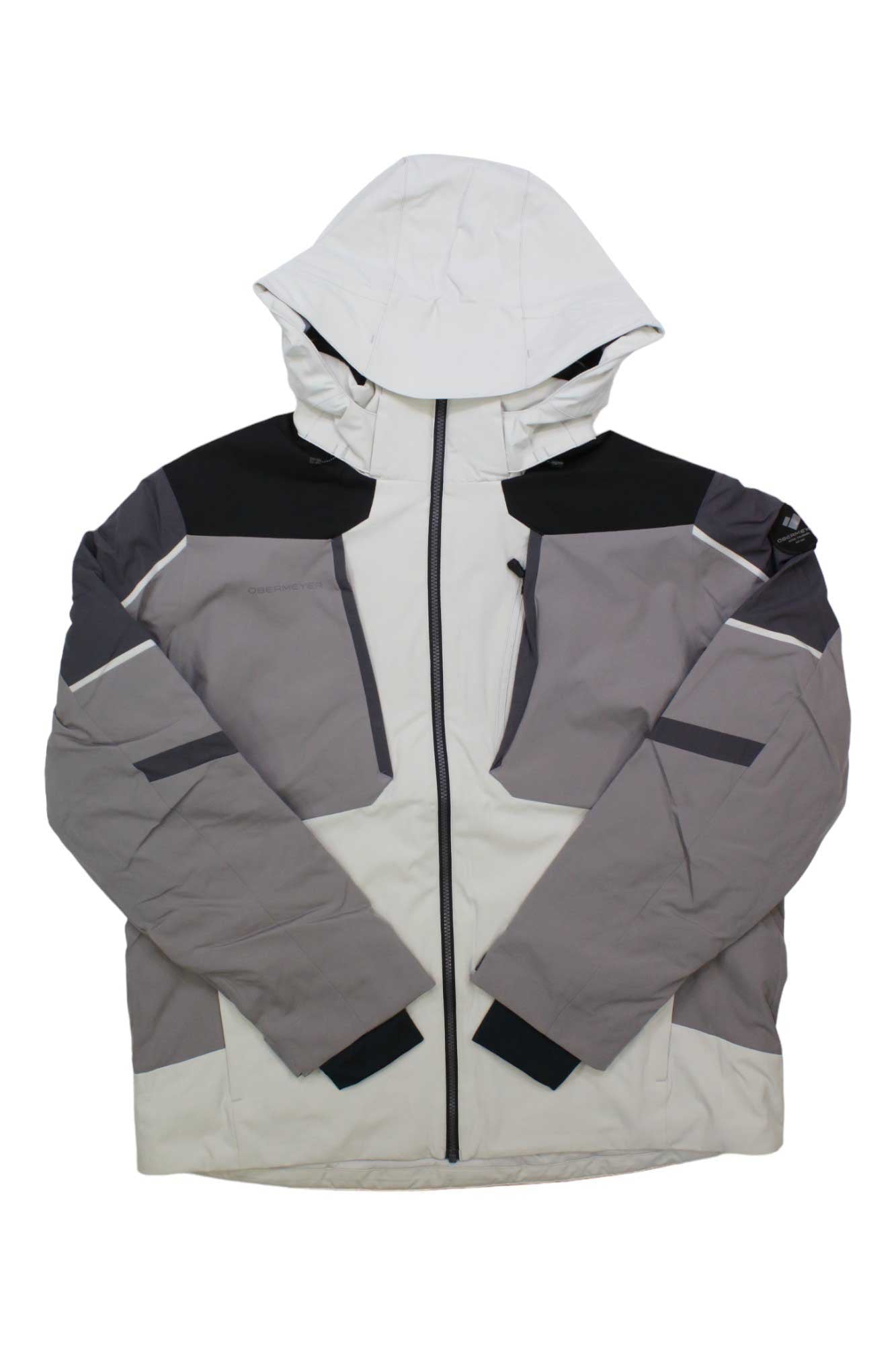 The Obermeyer Mens Foundation Jacket is a hooded ski jacket with a color block design in white, light gray, dark gray, and black accents, featuring a front zipper, multiple pockets, and made from recycled material.