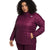 A woman with curly hair wears The North Face Womens Plus ThermoBall Eco 2.0 Jacket in quilted dark magenta, made from recycled nylon, hands in the pockets, standing against a plain white background.