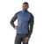 A man wearing a blue Smartwool Mens Smartloft Vest over a dark long-sleeve athletic shirt and black pants stands with one hand on his hip, looking slightly to the side against a plain white background.