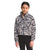 A young person with dark hair tied back is wearing The North Face Girls' Printed Osolita Full Zip Jacket, featuring a black and white print, paired with black leggings against a plain white background.