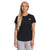 A woman with long blonde hair wears The North Face Womens Elevation SS Top in black, made from recycled polyester with moisture-wicking properties, and light gray pants, standing against a plain white background.