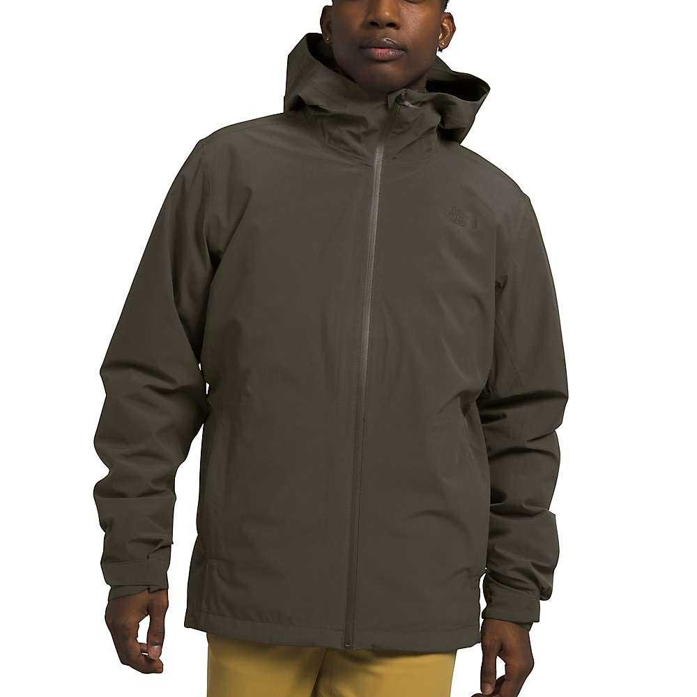 A person wears a dark olive green The North Face Mens Thermoball Eco Triclimate Jacket with a front zipper, long sleeves, and side pockets, paired with tan pants for a simple and functional outdoor adventure style.
