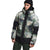 A person in The North Face Men's Corefire Down Windstopper Jacket in green and black camo with hood, wearing a black beanie and dark pants, stands against a plain background.