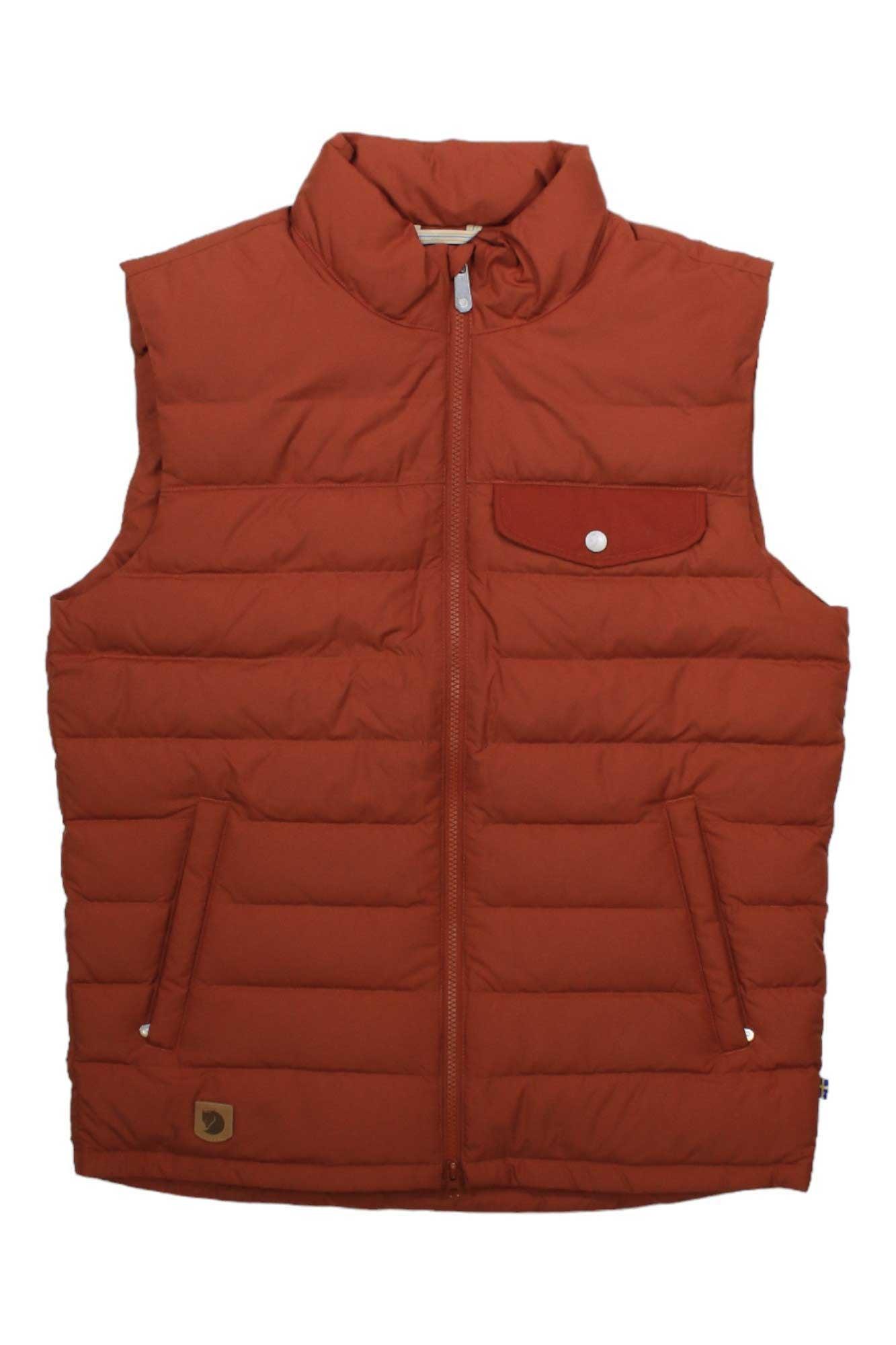The Greenland Down Liner Vest is a rust-colored, sleeveless puffer made from recycled polyester, featuring a high collar, front zipper, signature quilting, lightweight insulation, and a logo patch near the hem.