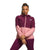 A person stands against a white background wearing The North Face Womens Mountain Sweatshirt Hoodie in pink and maroon with matching pants, arms crossed and a neutral expression.