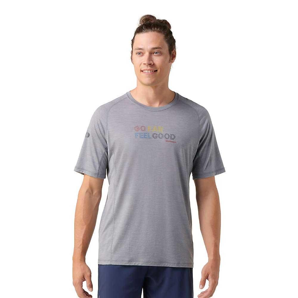 A man with long hair in a bun smiles while wearing the Smartwool Men's Active Ultralite Graphic SS Tee in light gray, featuring colorful "GO FAR FEEL GOOD" text. He stands looking slightly to the side.