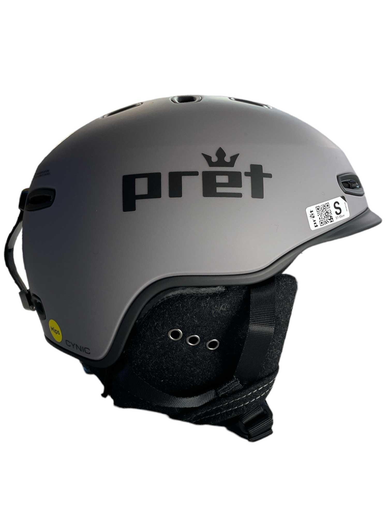 The Pret Men's Cynic X2 Ski Helmet features a matte gray finish, crown logo on the side, black ear covers and chin strap, adjustable venting with ventilation holes, plus a QR code sticker near the back.