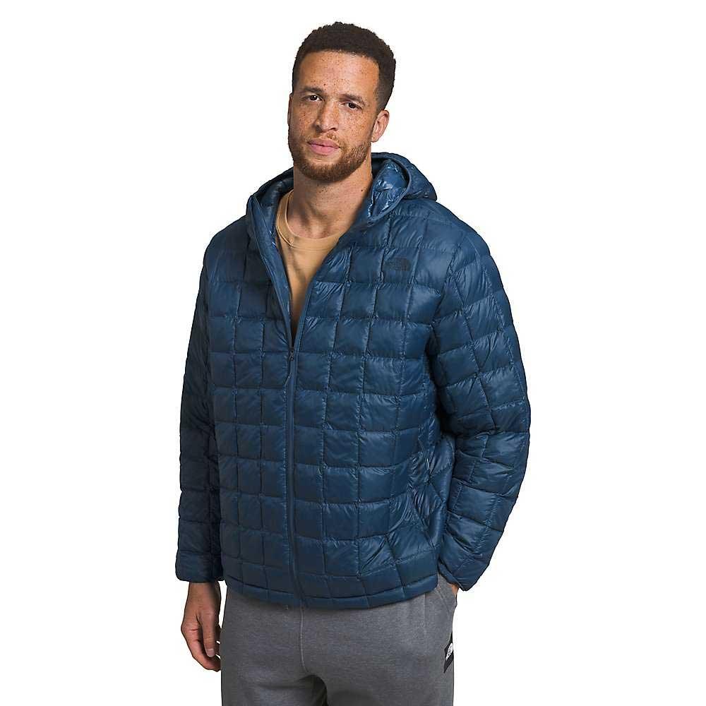 A man in The North Face Men's Big Thermoball Eco 2.0 Hoodie made from recycled nylon and gray sweatpants stands facing forward with a neutral expression against a plain white background.