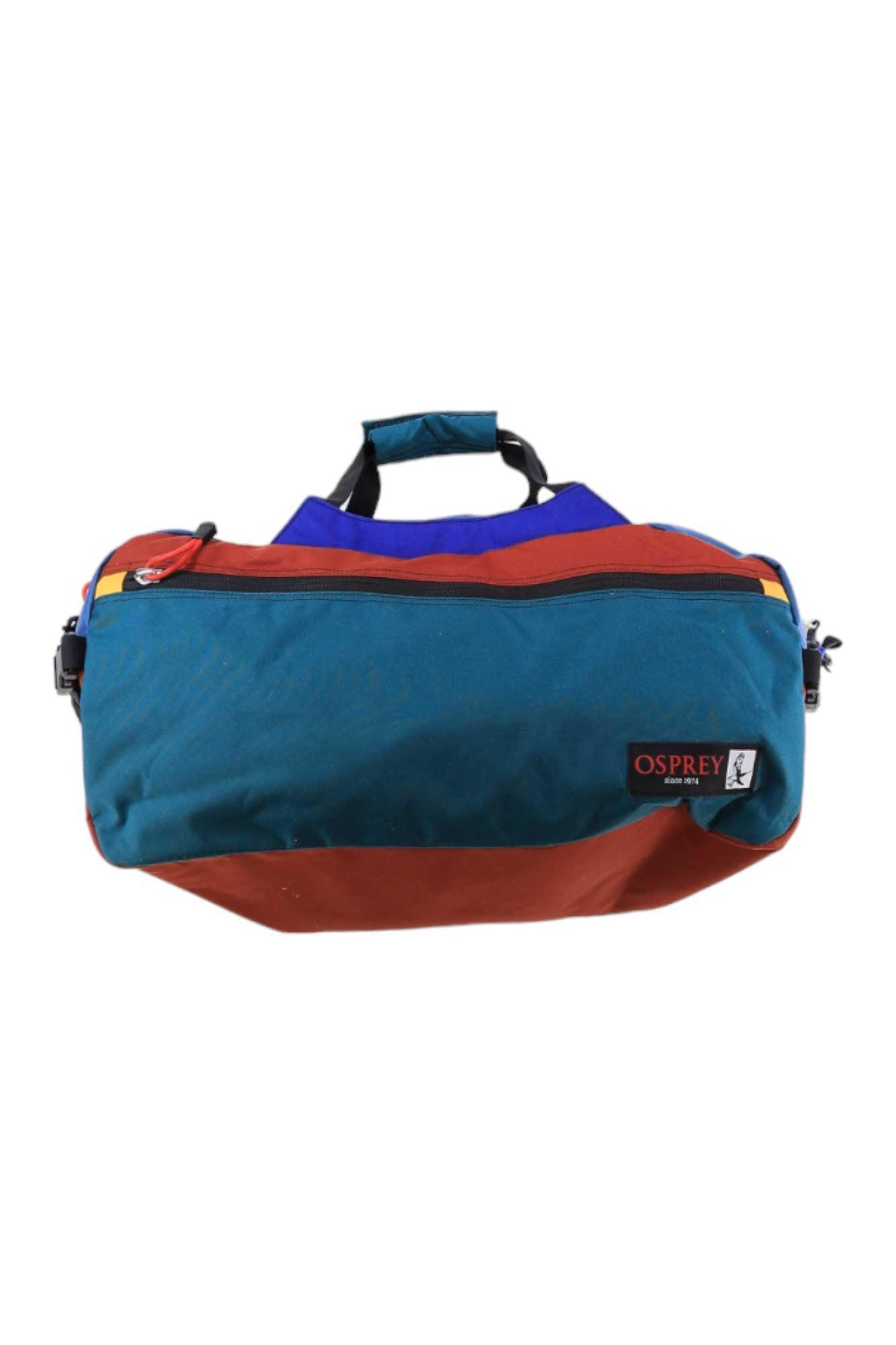 The Osprey Heritage Transporter 45 Duffle Bag features teal, rust orange, and blue recycled nylon panels, black zippers and handles, and a red, black, and white logo patch on the front.