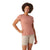 A woman with curly hair smiles while wearing the Smartwool Women's Merino Sport 150 Tee in light pink and beige shorts—ideal for women's fitness—against a white background.