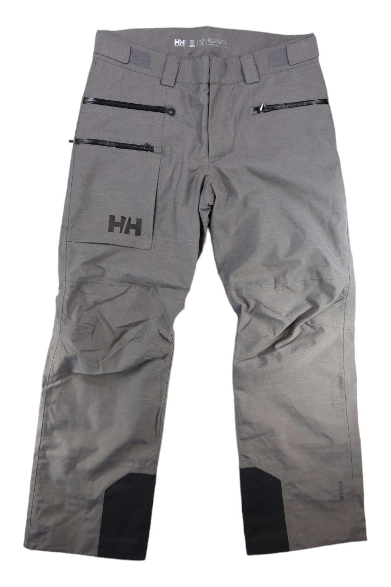 Helly Hansen Mens Garibaldi 2.0 Pant in gray, featuring black zipper thigh pockets, reinforced cuffs, belt loops, and the HH logo on the left pocket. These men's ski pants are displayed flat on a white background.