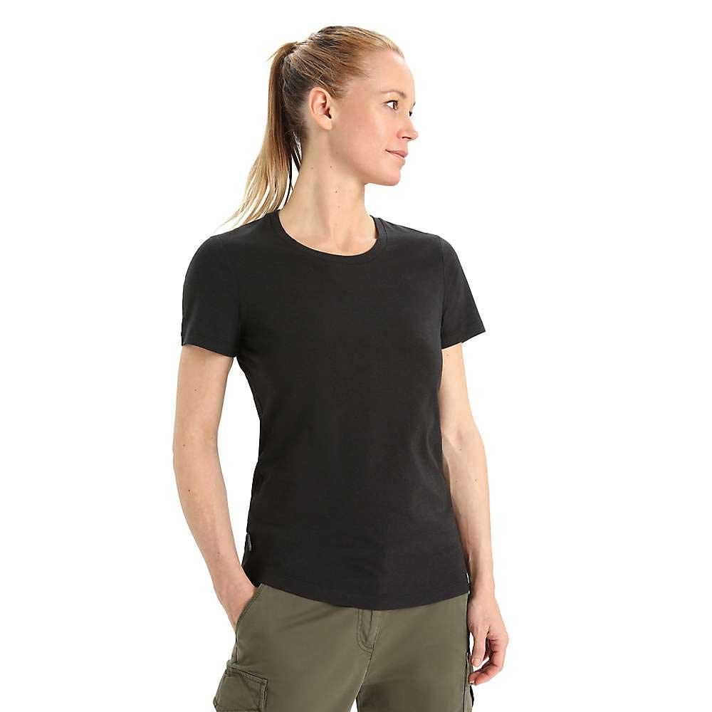 A woman with blonde hair in a ponytail wears an Icebreaker Womens Central Classic SS Tee in plain black and olive green cargo pants, standing against a white background and looking slightly to her left.