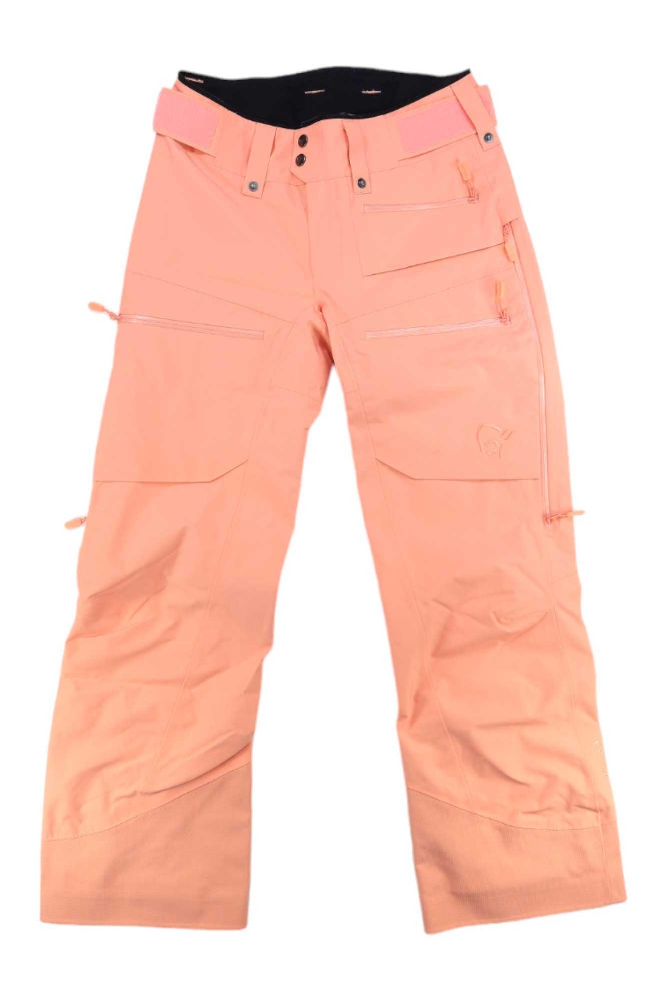 Norrona Womens Lofoten GORE-TEX Insulated Snow Pants in peach, featuring multiple zippered pockets, belt loops, reinforced knees, and adjustable waist tabs, shown laid flat on a white background.