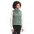 A woman with curly hair wears The North Face Women's Cragmont Fleece Vest in sage green over a cream long-sleeve shirt and black pants, standing and smiling slightly while looking to the side.