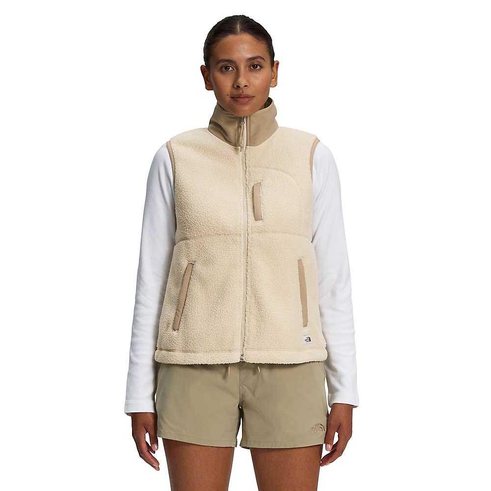 A person stands facing forward, wearing The North Face Women's Cragmont Fleece Vest over a white long-sleeve shirt and khaki shorts, against a plain white background.