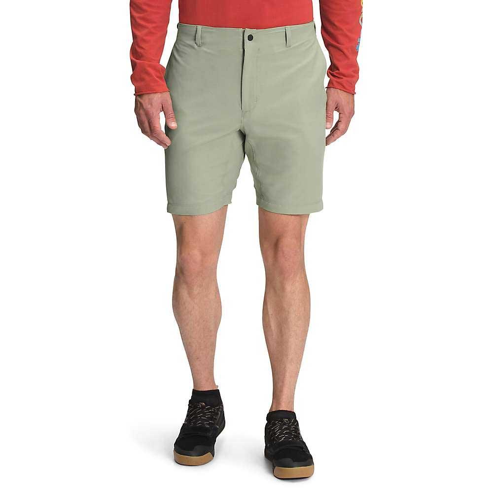 A person wearing The North Face Men's Project 8 Inch Short in light green, a red long-sleeve shirt, and black sneakers stands facing forward against a white background.