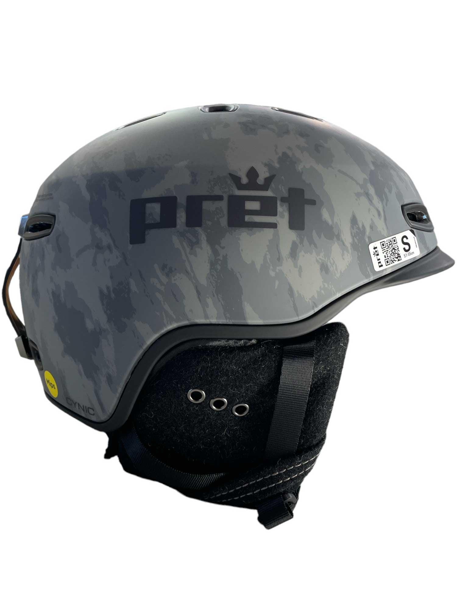 The Pret Men's Cynic X2 Ski Helmet features a gray camo pattern, ear protection, adjustable venting, ventilation holes, a chin strap, and a size S sticker on the side.