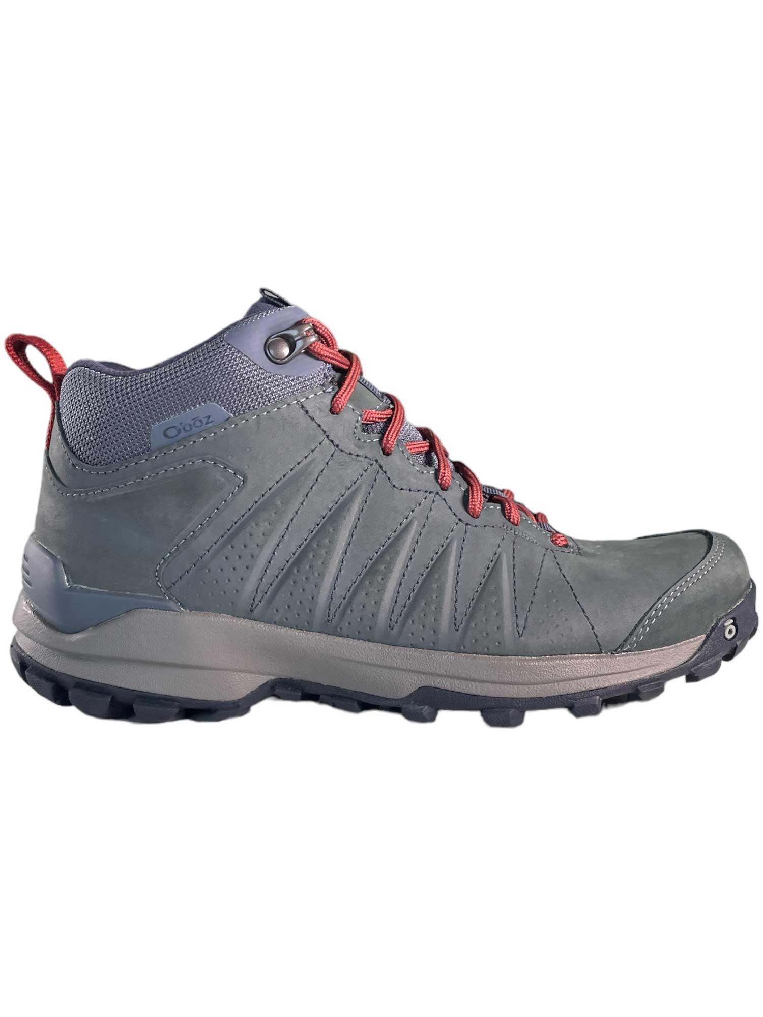 The Oboz Women's Sypes Mid Leather B-Dry Shoe in gray features red laces, a rugged black sole, and a red pull tab—sustainable hiking boots built for outdoor adventures.