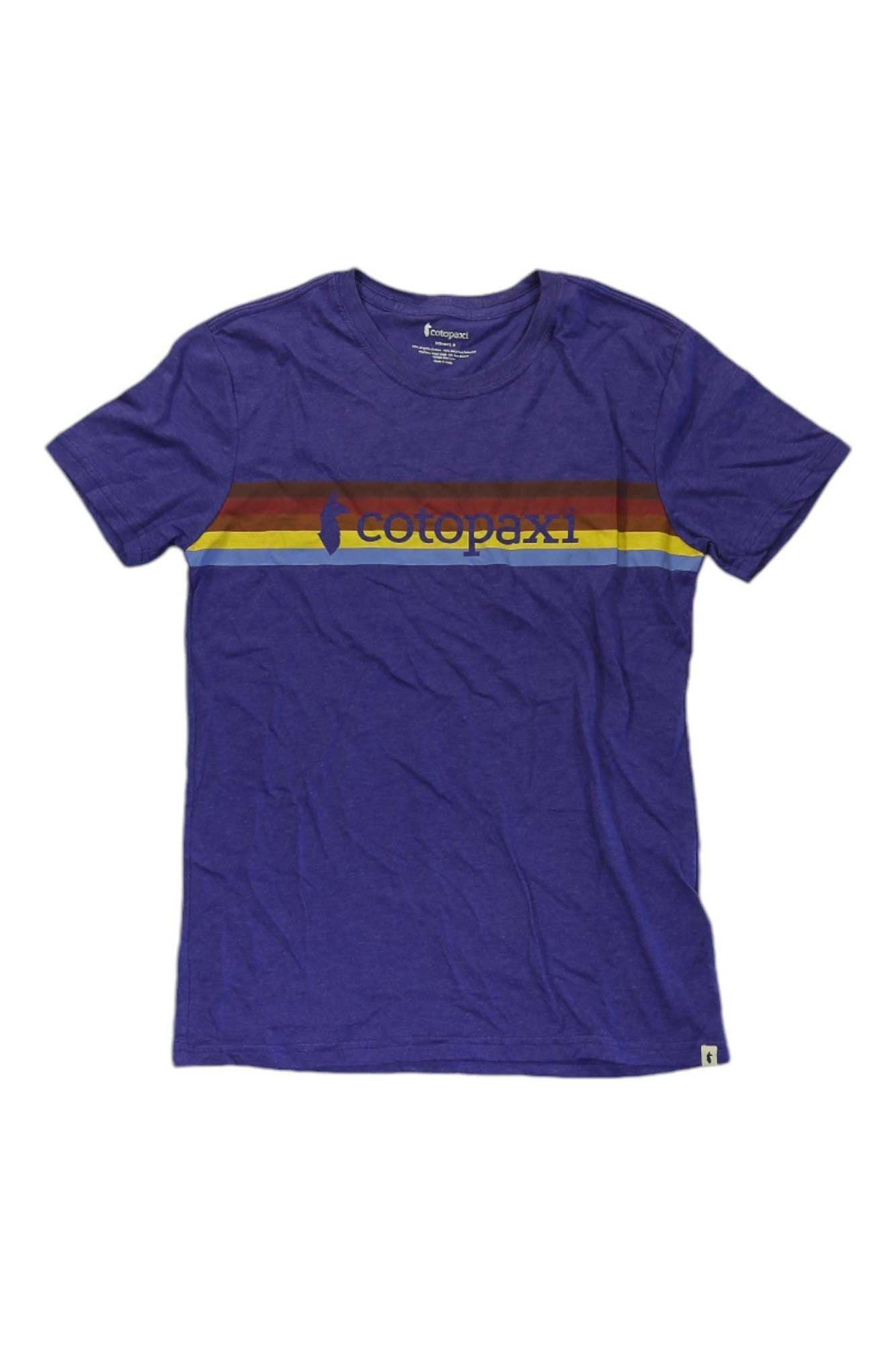 The Cotopaxi Womens On The Horizon T-Shirt is a purple organic cotton tee with a red, orange, and yellow horizontal retro stripe on the chest and the blue Cotopaxi logo and name printed on the front.