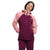 A person stands with hands in pockets against a white background, wearing The North Face Women's Valle Vista Jacket featuring a hood, light pink sleeves, and a dark magenta body and pants.