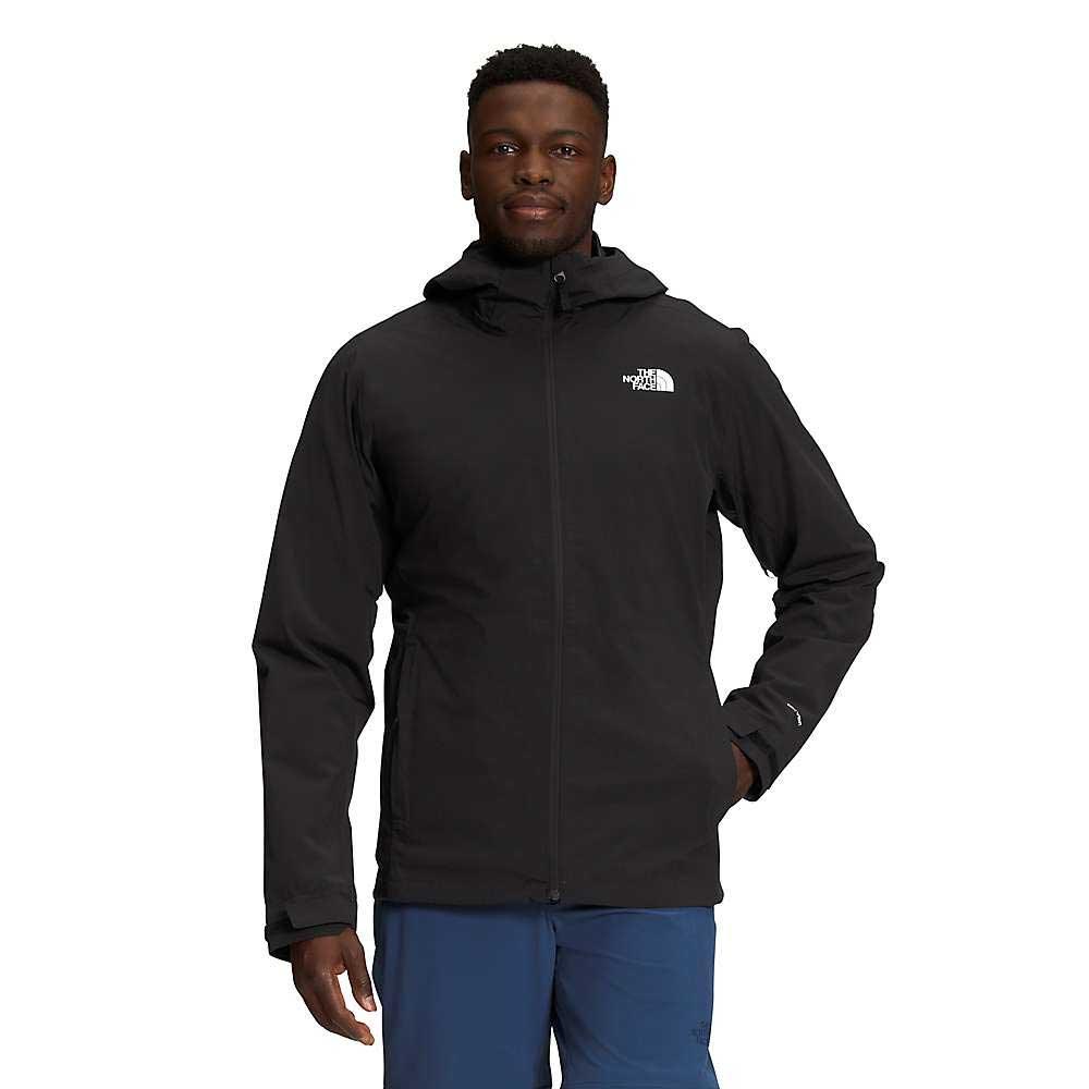 A man stands facing forward with one hand in his pocket, wearing a black The North Face Mens Thermoball Eco Triclimate Jacket and blue pants against a plain white background.