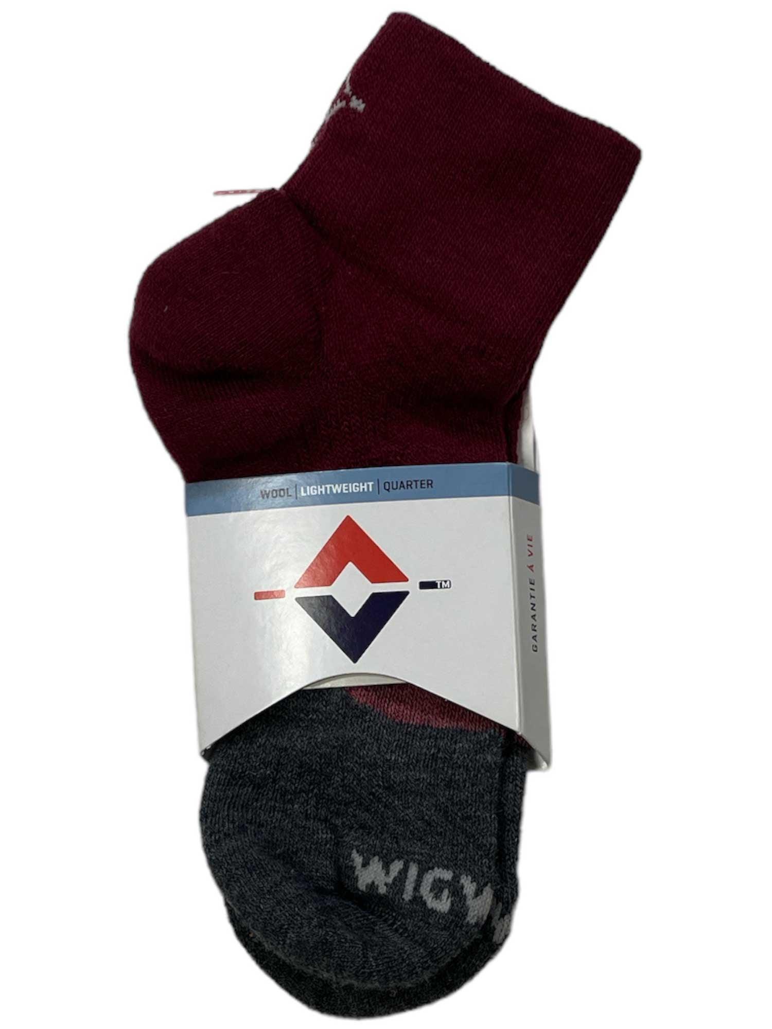 A pair of socks, one maroon and one dark gray, are folded with a white label displaying a geometric logo and text. The gray Wigwam Trail Junkie Light Quarter Sock features "WIGWAM" near the toe for comfort every step.