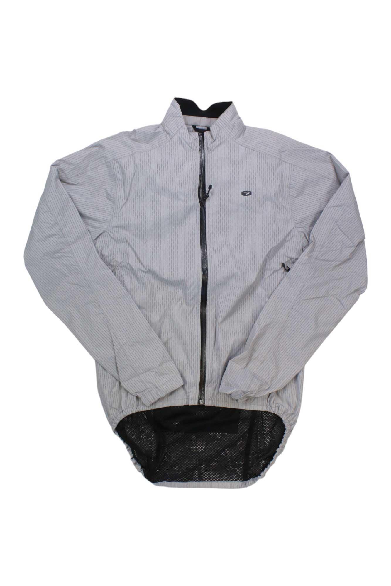 The Sugoi Men's Zap Bike Jacket is light gray with a subtle checkered pattern, windproof and waterproof fabric, front zipper, high collar, small chest logo, and an extended mesh hem at the back. Shown laid flat on a white background.