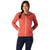 A woman smiles at the camera, wearing the Smartwool Women's Merino Sport Ultra Light Hoodie in coral over a dark top and navy pants, standing with hands on hips against a white background.
