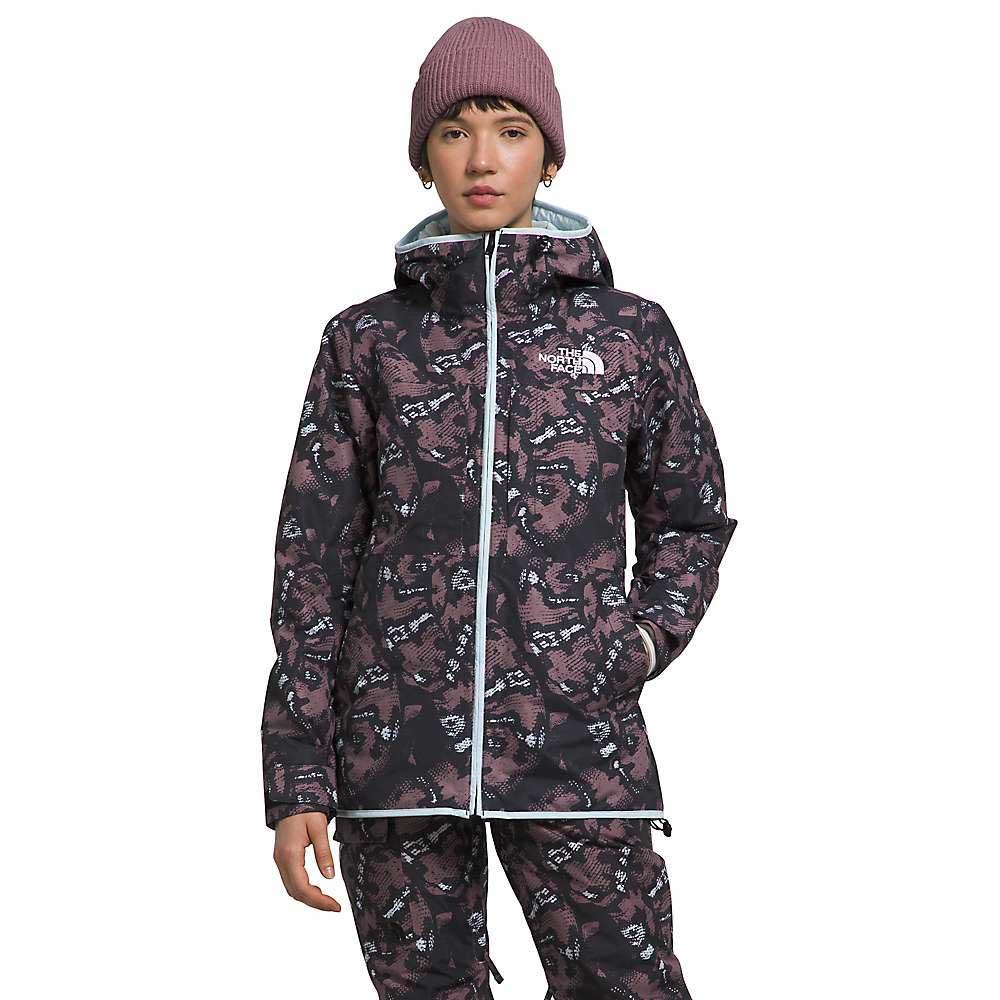 A person wears The North Face Womens Namak Insulated Jacket and matching pants, hood up, with a pink beanie. The jacket has a pattern, white zipper, visible logo on the chest, and is waterproof—ideal for winter.