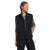 A woman wears The North Face Women's Cragmont Fleece Vest in black over a long-sleeve green shirt and black pants, standing with one hand in her pocket, looking to the side and smiling slightly.